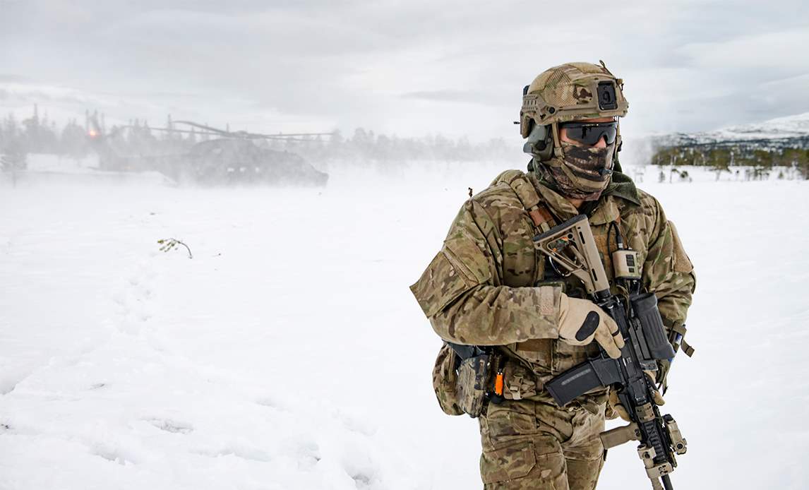 Soldat foran helikopter af typen EH101 i snedækket landskab.